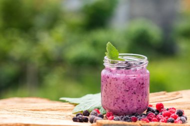 Yeşil bahçe arka planının üzerinde tahta tahtada farklı meyveler içinde tatlı yoğurt.