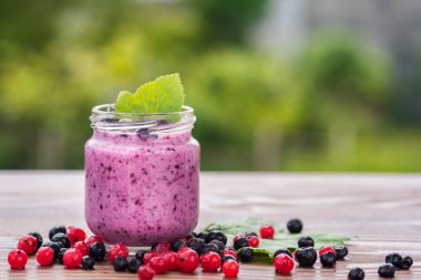 Yeşil bahçe arka planının üzerinde tahta tahtada farklı meyveler içinde tatlı yoğurt.