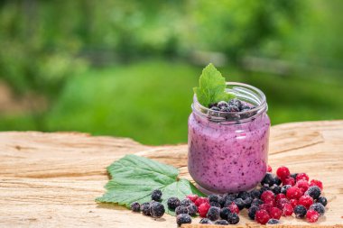 Yeşil bahçe arka planının üzerinde tahta tahtada farklı meyveler içinde tatlı yoğurt.