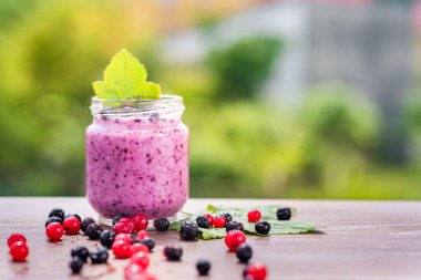 Yeşil bahçe arka planının üzerinde tahta tahtada farklı meyveler içinde tatlı yoğurt.
