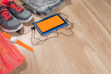 Ahşap arka planda birkaç giysi ve aksesuar içeren bir tablet.