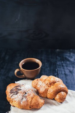 Siyah ahşap arka planda tatlı kruvasanlar ve bir fincan kahve. Boşluğu kopyala
