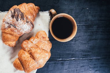 Siyah ahşap arka planda tatlı kruvasanlar ve bir fincan kahve. Boşluğu kopyala