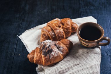 Siyah ahşap arka planda tatlı kruvasanlar ve bir fincan kahve. Boşluğu kopyala