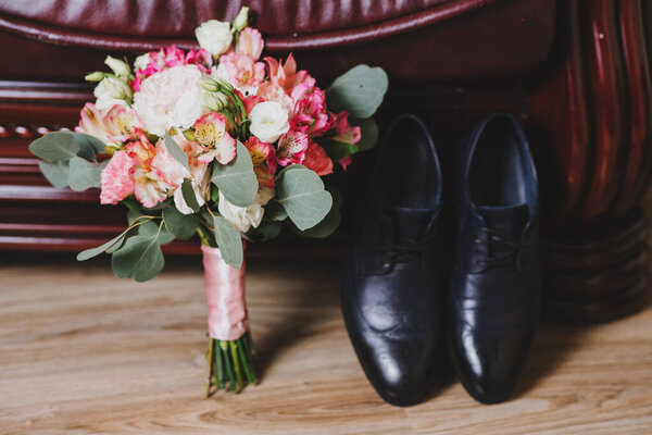 Groom shoes with wedding bouquet on wooden background