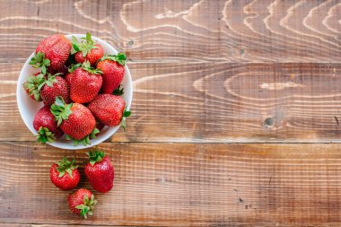 Tahta arka planda beyaz tabakta olgun tatlı çilekler. Boşluğu kopyala