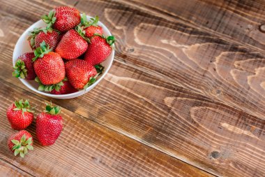 Tahta arka planda beyaz tabakta olgun tatlı çilekler. Boşluğu kopyala