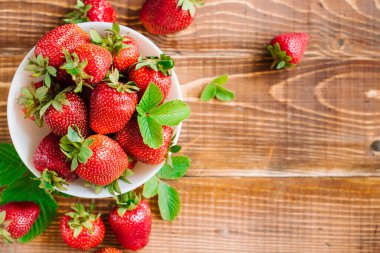 Tahta arka planda beyaz tabakta olgun tatlı çilekler. Boşluğu kopyala