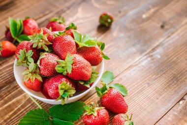 Tahta arka planda beyaz tabakta olgun tatlı çilekler. Boşluğu kopyala