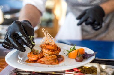 Bir aşçı sosun altında karideslerle lezzetli yemekler hazırlıyor.