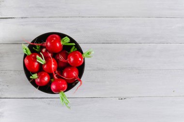 Beyaz ahşap arka planda siyah tabakta taze kırmızı turp.