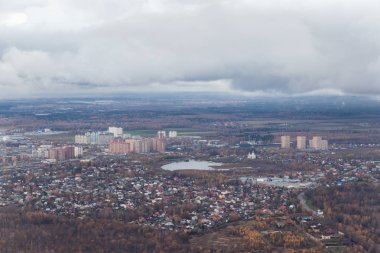 Uçağın yükseklikten küçük bir şehir. Göl yakınındaki yüksek binalar. Dünya'dan bir uçak görünümünü. Beyaz bulutların altında road, endüstriyel binalar ile orman üst kısmında.