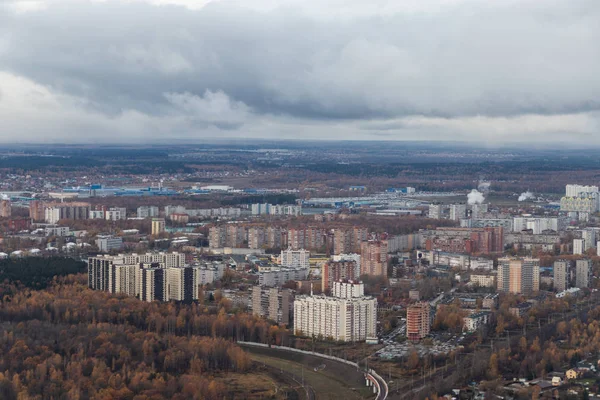 High-rise buildings near the road. A small city with an altitude of the aircraft. At the top of the white clouds on the horizon, below the forest with the road, city buildings.