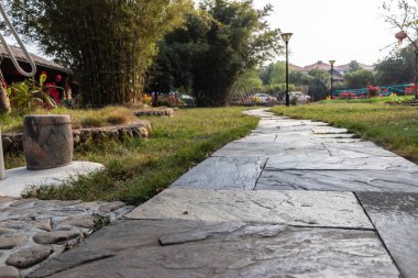 Doğal bir taş bir bahçe yolundan. Yeşil çim, ağaçlar, dağlar. Kahverengi kare taş döşeli.