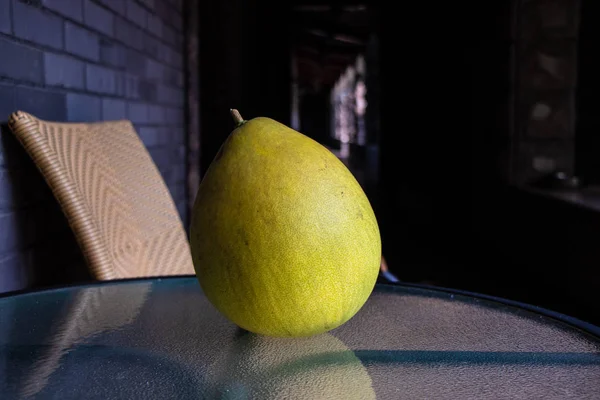 Large yellow fruit Pomelo. Fruit closeup lies on the glass table. Gray brick wall. Big beautiful Pomelo.