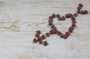 Kalp kahverengi gül yapılan bir okla deldi. Ahşap arka plan üzerinde bokeh fotoğraf. Aşk, Sevgililer Günü Bayramı. Kartpostal kopya alanı ile.