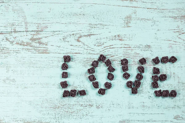 Ahşap arka plan, üstten görünüm üzerinde kahverengi gül koyu kahverengi aşk mektupları. Ahşap arka plan üzerinde metin aşk. Tatil sevgili için tebrikler.