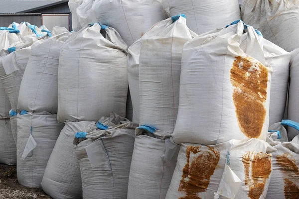 Large white bags with blue ribbon inside the salt lie on the street. Industrial fertilizers are stored in bags in a heap. Rusty stains on the package.