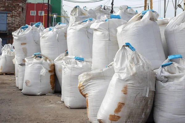 Büyük beyaz tuz torbaları sokakta yatıyor. Endüstriyel gübreler torbalarda bir yığın halinde saklanır. Pakette paslı lekeler.