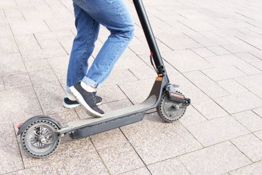 Kız elektrikli bir scooter'a biniyor, ayağıyla itiyor. Teknolojik çevre dostu ulaşım. Modern aktif kentsel yaşam tarzı.