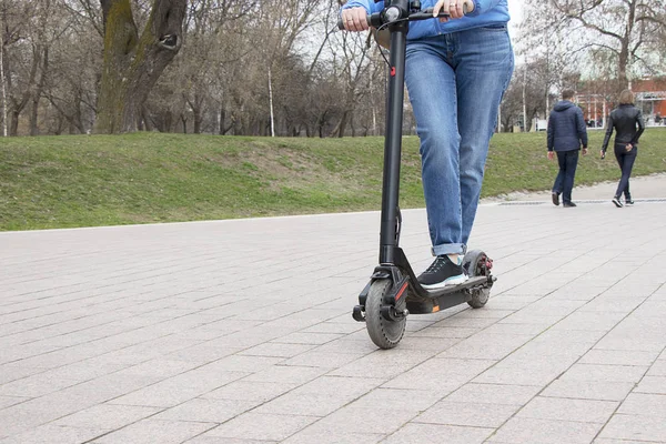 Chica montando un scooter eléctrico en el parque en un camino de piedra con una cámara de acción. Transporte tecnológico respetuoso con el medio ambiente. Estilo de vida urbano activo moderno . —  Fotos de Stock