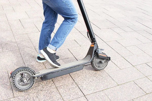 Kız elektrikli bir scooter'a biniyor, ayağıyla itiyor. Teknolojik çevre dostu ulaşım. Modern aktif kentsel yaşam tarzı.