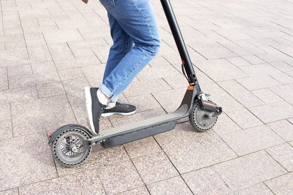 Chica en vaqueros azules montando un scooter eléctrico. Electro scooter de transporte ecológico tecnológico. Estilo de vida urbano activo moderno . —  Fotos de Stock