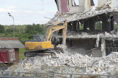 Sarı ekskavatör bir kamyonüzerine yükleme için inşaat atıkları alır. Teknik bina yıkıldı, takviye, beton ve taşlar olduğunu. Yıkılmış ev, beton, bağlantı parçaları, toz sinekleri.