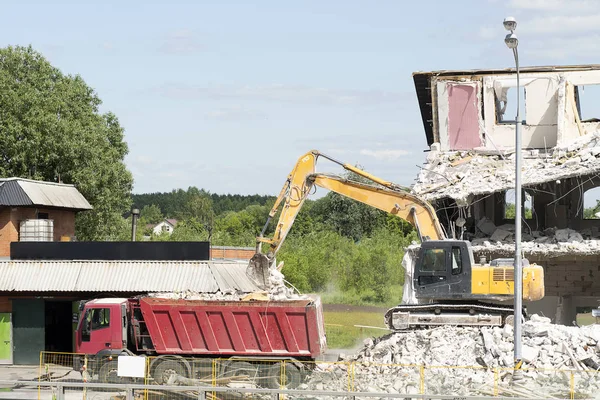 Sarı ekskavatör, inşaat enkazını kamyona yükler. Teknik bina yok, parçaları, beton ve taşlar olduğunu. Ekskavatör kovası bir kamyonun arkasına enkaz döker. Karayolu
