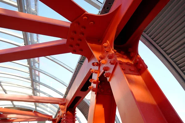 Poutres de fer rouge boulonnées. Connexion angulaire de plusieurs poutres de fer en un seul endroit. Traversée piétonne avec construction en fer et plafond en verre . — Photo
