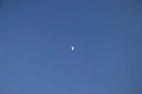 Połowa księżyca na jasnym błękitnym niebie w godzinach popołudniowych. Mały satelita ziemi RA monofoniczne tle. Popołudnie księżyca. — Zdjęcie stockowe