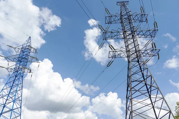 Kablolu iki elektrik yüksek gerilim diremi. Güçlü elektriğe sahip metal bir direk. Gökyüzü beyaz bulutlarla mavi..
