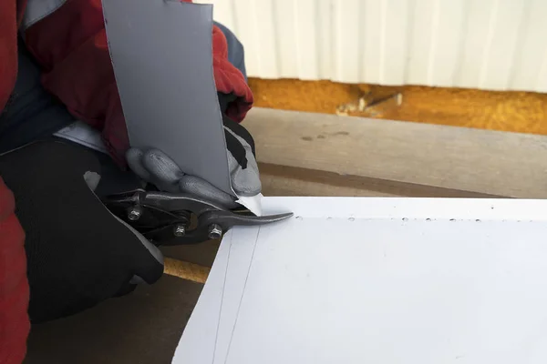 stock image Builder with scissors cuts a white steel sheet. A working tinsmith cuts out an iron roof at a mark.