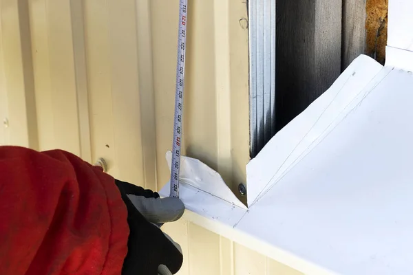 Um artesão enluvado mede a janela do lado de fora com uma fita métrica. Construtor profissional com uma ferramenta mede a distância . — Fotografia de Stock