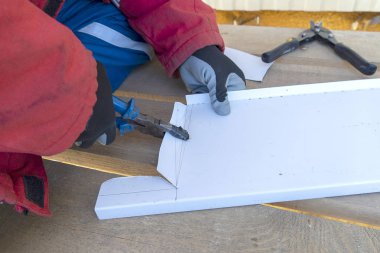 Yükseklikteki inşaatçı bir metal levhayı büker. Çalışan bir el, çatı demirini pliers ile bir aletle büker..