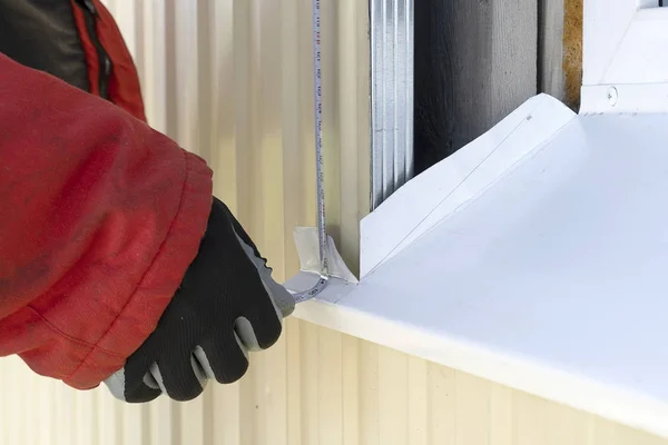 Um artesão enluvado mede a moldura da janela com uma fita métrica. Ferramenta profissional construtor mede a distância da janela . — Fotografia de Stock