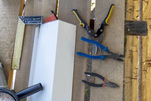 Ferramentas de construção rebarbadora, régua de medição de ângulo, alicate, tesoura de ferro, broca, fita métrica. No andaime de madeira encontra-se uma ferramenta de trabalho . — Fotografia de Stock