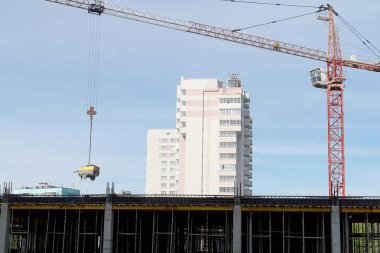 Bir inşaat vinci bir alet taşıyor. Yüksek katlı bir binanın yapımında bom vinç. Sapanlı vinç kancası kaynak makinesini tutar.              