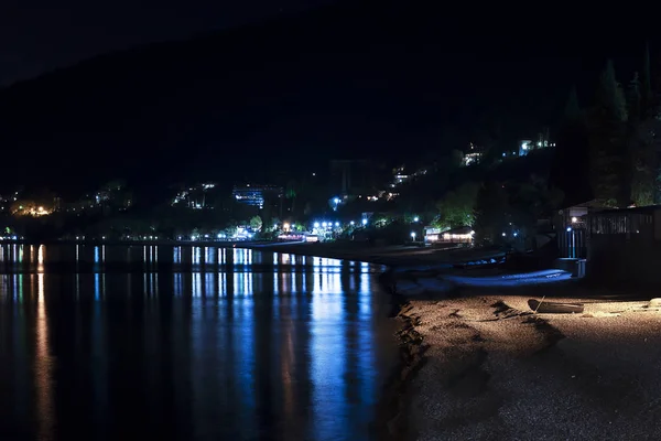 Città di notte nel riflesso dell'acqua del mare. Notte nera, altopiani, Abkhazia, turismo, viaggi, paesaggio urbano notturno . — Foto Stock