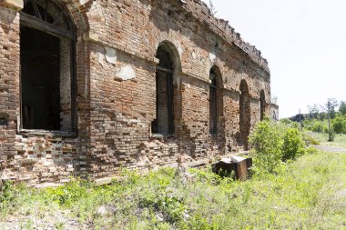 Eski harap kırmızı tuğla bina. Kemerli pencereler boş, çatıda çimler büyüyor, geniş yığma duvarlar.