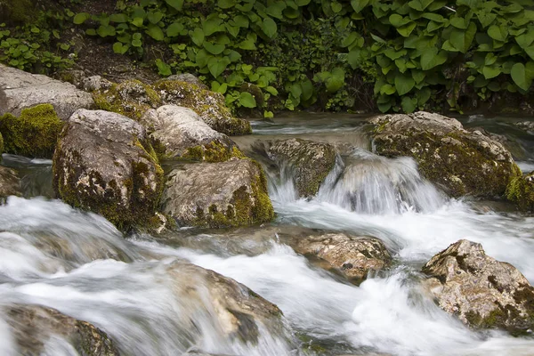 A stream of water flows over stones with green moss, naturalness in nature. Small picturesque waterfall on the stones.