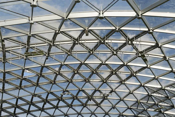 Futuristic metal and glass roof design. Modern ceiling with elements of glass, metal mesh. Blue sky.