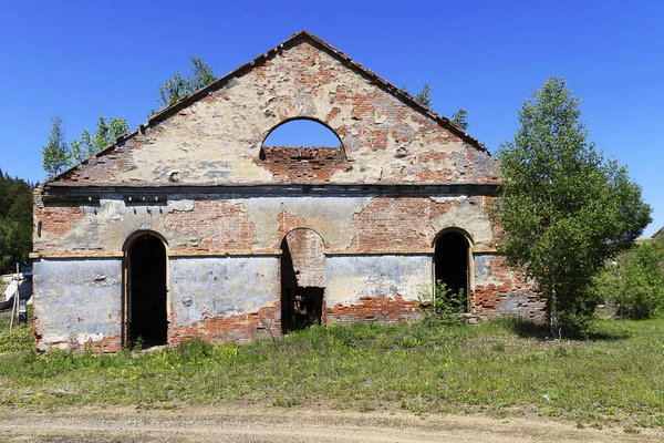 Ruined old red brick building. Wall of an old factory with semicircular arches in the summer on a sunny day. There are trees on the roof. — Stock Photo, Image