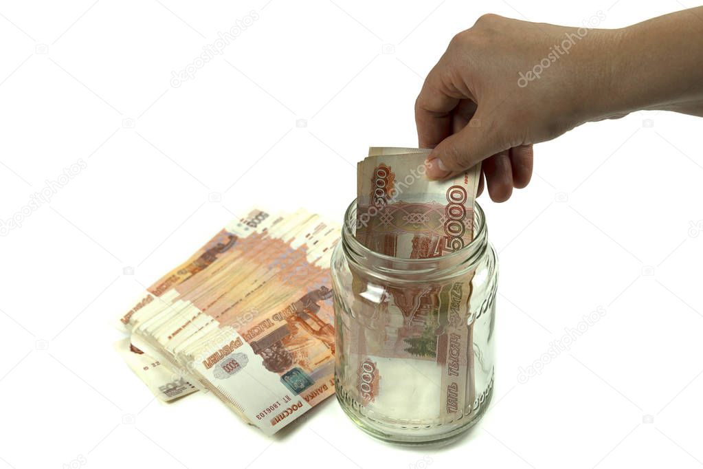 Hand puts Russian money in a glass jar. On a white background, a bundle of banknotes with a face value of five thousand rubles.