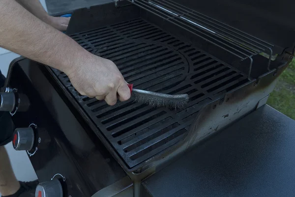 Een man borstels een straat zwarte grill met een ijzeren borstel. Grill bereiding voor het braden van vlees. — Stockfoto