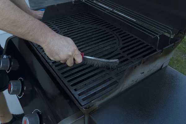 Un uomo spazzola una griglia nera di strada con una spazzola di ferro. Preparazione alla griglia per friggere la carne . — Foto Stock