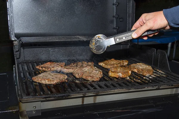 Op de barbecue worden sappige smakelijke stukjes vlees gekookt. Het vlees wordt gegrild. De mannelijke hand draait de stukjes vlees met Tang. — Stockfoto