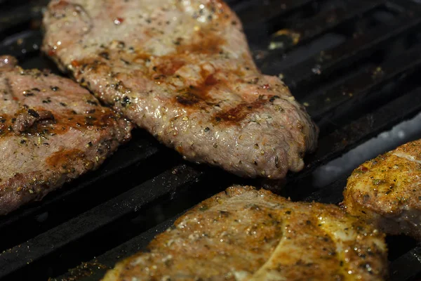 La carne de cerdo marinada con especias se asa en una parrilla de gas de hierro negro. Juicy pieces of beef meat closeup cooked on a barbecue . — Foto de Stock