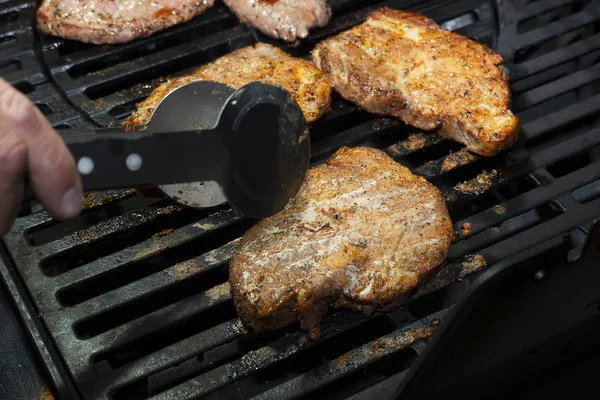Mão vira um pedaço de carne suculenta, que é cozido na grelha. Churrasco no gás, deliciosa carne grelhada . — Fotografia de Stock
