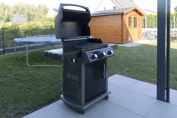 Een grote zwarte Gasgrill staat op de straat op het gazon in de buurt van het huis. Straat koken. — Stockfoto